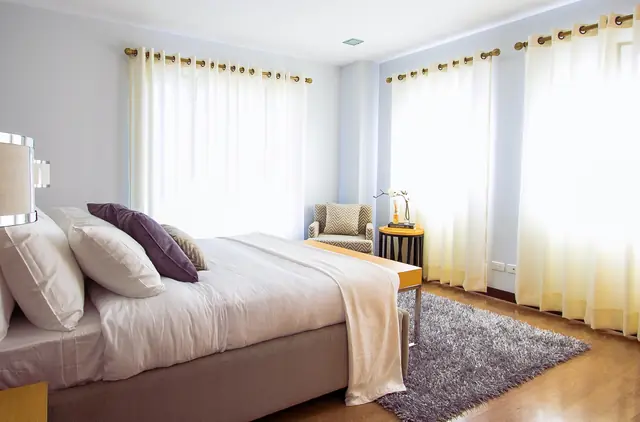 Habitación de hotel con cama de sábanas blancas y cortinas claras